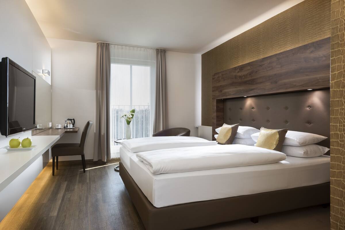A modern hotel room with a large bed, a flat-screen TV, a desk, and a view of the city.