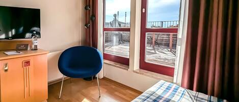 Habitación de hotel con cama, escritorio con televisor, una silla y ventana con vista a un muelle.