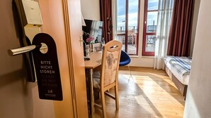 Een hotelkamer met een houten vloer, een eettafel met stoelen, een bed met een gestreept dekbed en een balkon met rode gordijnen.