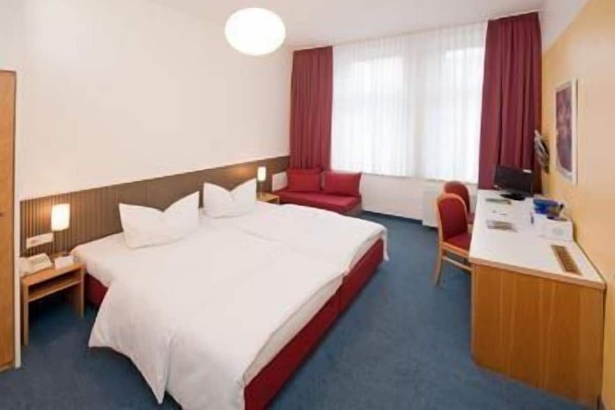 Quarto de hotel com uma cama grande, uma escrivaninha e uma cadeira.