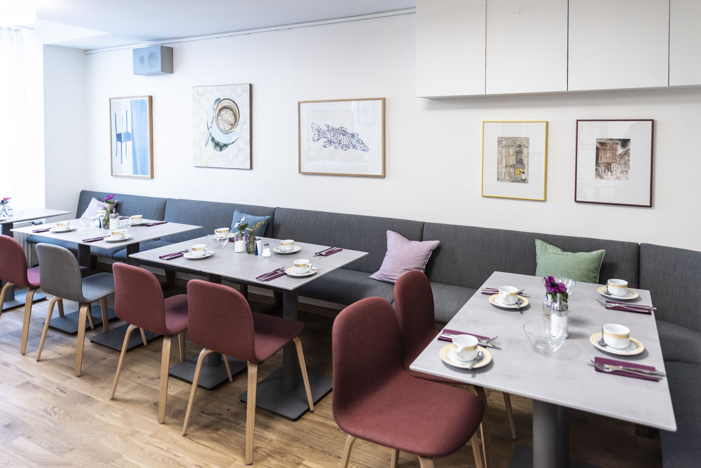 A modern dining area with tables set for four, each with a vase of flowers, plates, and cutlery.
