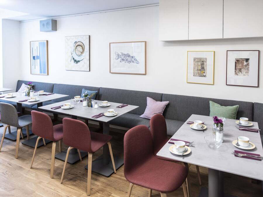 A modern dining area with tables set for four, each with a vase of flowers, plates, and cutlery.