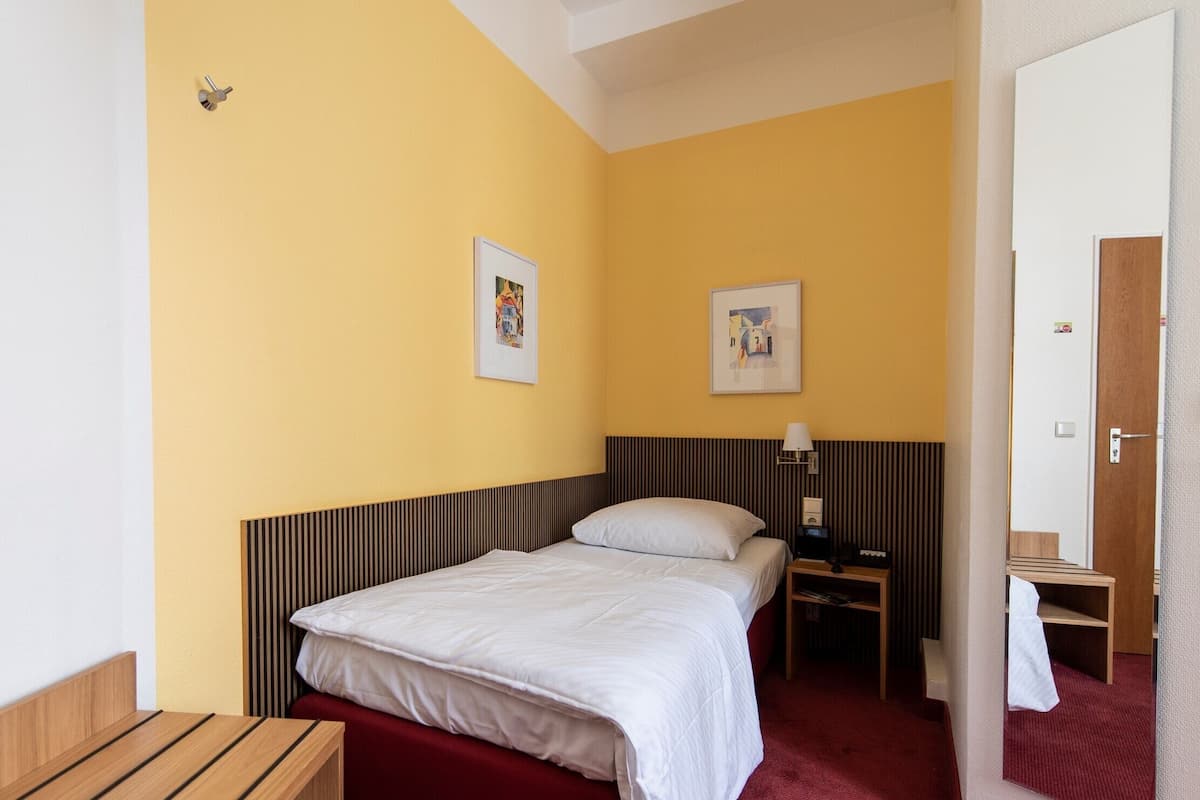 Quarto de hotel com cama, mesa de cabeceira, luminária e espelho.