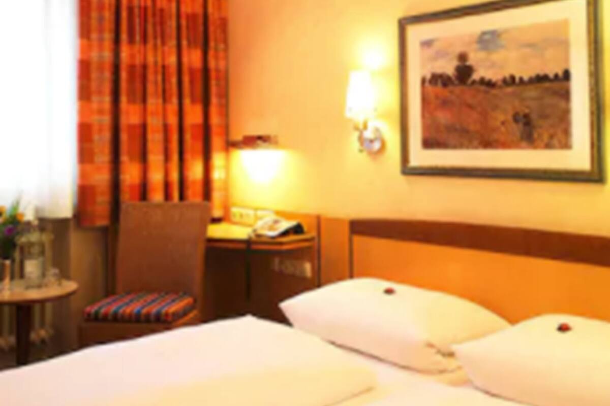 A hotel room with a bed, a chair, a table with a lamp, and a painting on the wall.