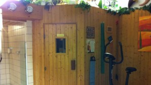 A wooden room with a door, a small window, and an exercise bike. - Hotel Hauser (Munich)