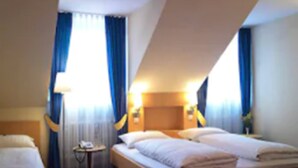 A hotel room with a large bed, a smaller bed, a bedside table with a lamp, and a window with curtains. - Hotel Hauser (Munich)