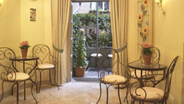 A room with four metal-framed chairs and tables, a large window with curtains, a small potted plant, and a wall-mounted light fixture. - Hotel Hauser (Munich)