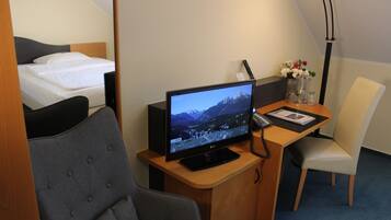 Une chambre d’hôtel comprenant un lit, un bureau avec un écran d’ordinateur, une chaise et une lampe de bureau.