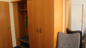 Een kamer met een houten garderobe, een grijs gestoffeerde fauteuil en een spiegel die een deel van de kamer weerspiegelt.