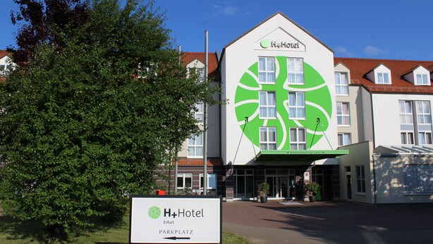 A hotel with a distinctive green logo, a sign indicating 'Erfurt Parkplatz', and a clear view of the entrance. - H+ Hotel Erfurt (Erfurt)
