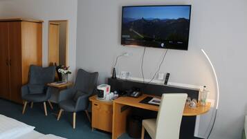 Habitación de hotel con cama, dos sillones, escritorio con computadora, televisor montado en la pared y una mesita de noche con lámpara.