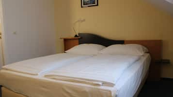 A neatly made twin bed with white linens, a bedside table with a lamp, and a framed picture on the wall.
