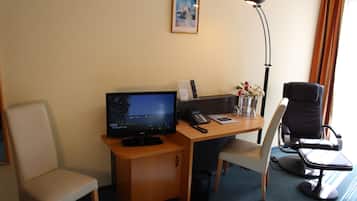 Quarto de hotel com escrivaninha, televisão, cadeira e abajur.