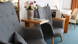 A modern hotel room with grey upholstered chairs, a wooden side table with a book and a vase of flowers, and a desk with a computer and a lamp. - H+ Hotel Erfurt (Erfurt)