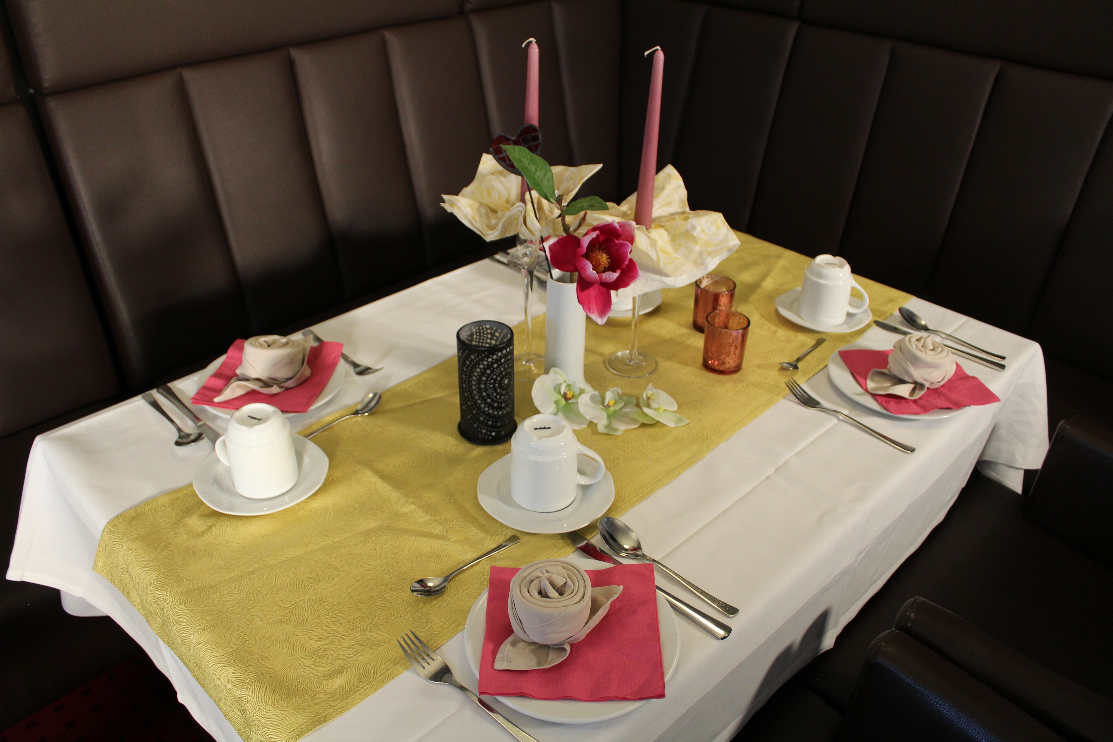 A dining table set with white and pink napkins, silverware, and a vase with flowers.