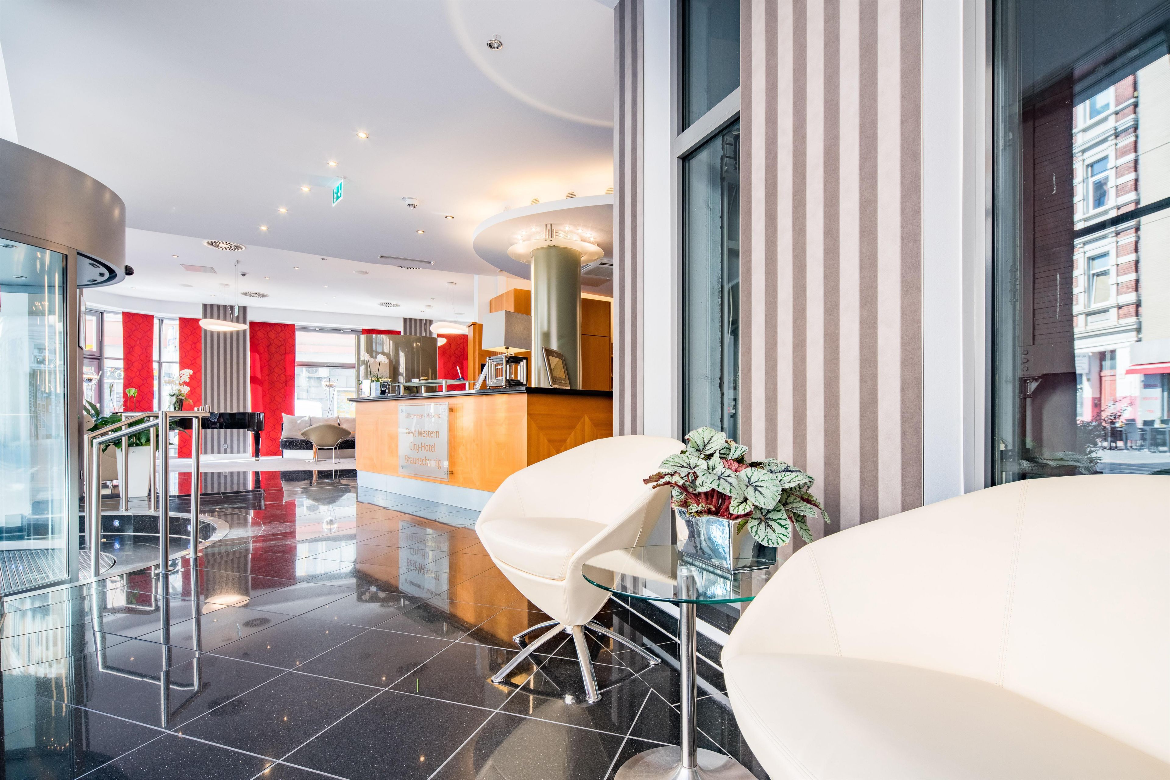 En moderne hotellobby med reception, siddeområde og udsigt over byen.