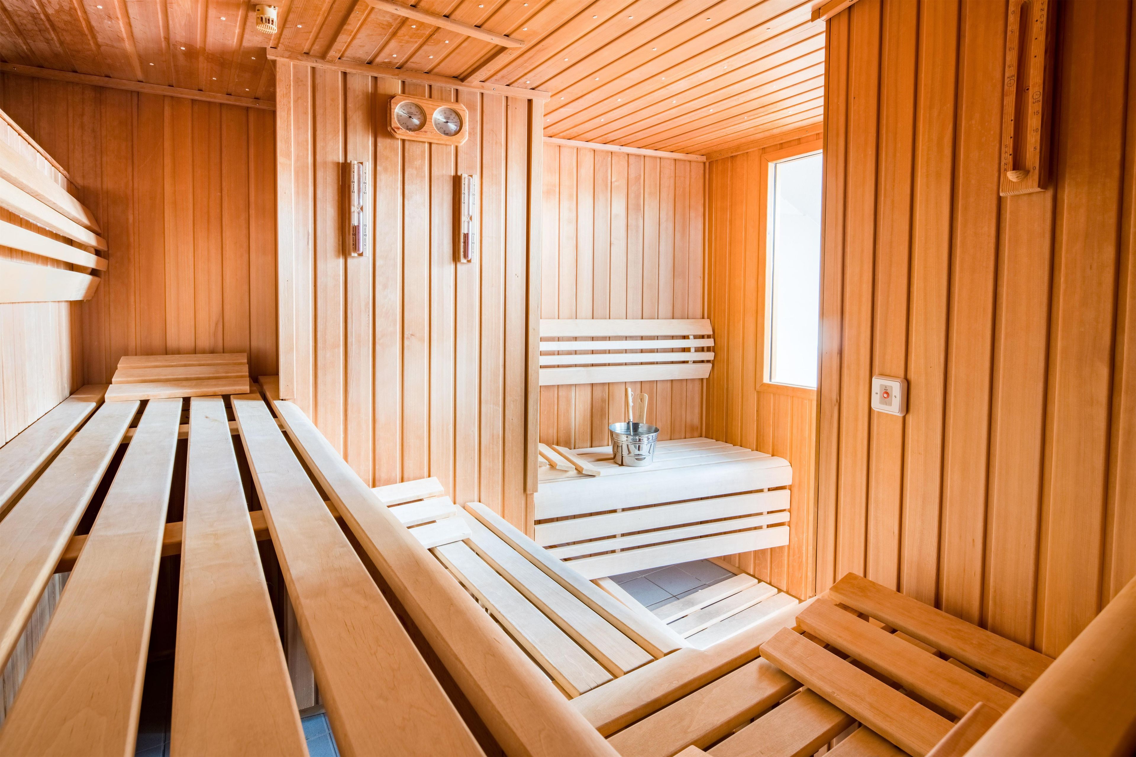 Una sauna con bancos de madera y una pequeña mesa con un cubo y palos de madera.