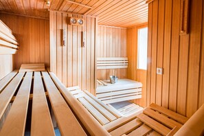 A sauna with wooden benches and a small table with a bucket and wooden sticks.