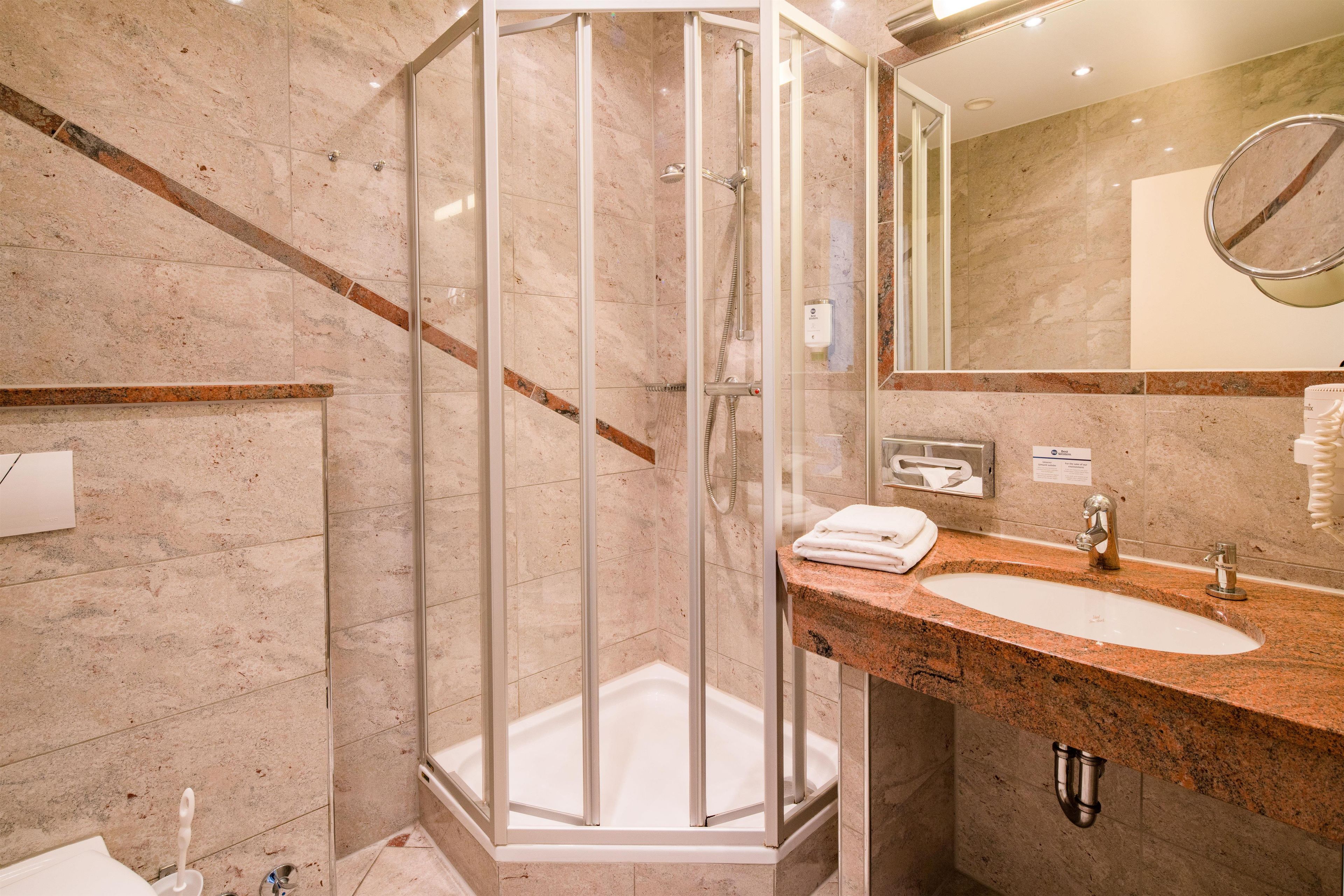 A modern bathroom with a glass-enclosed shower, a marble-tiled wall, a sink with a granite countertop, and a mirror.