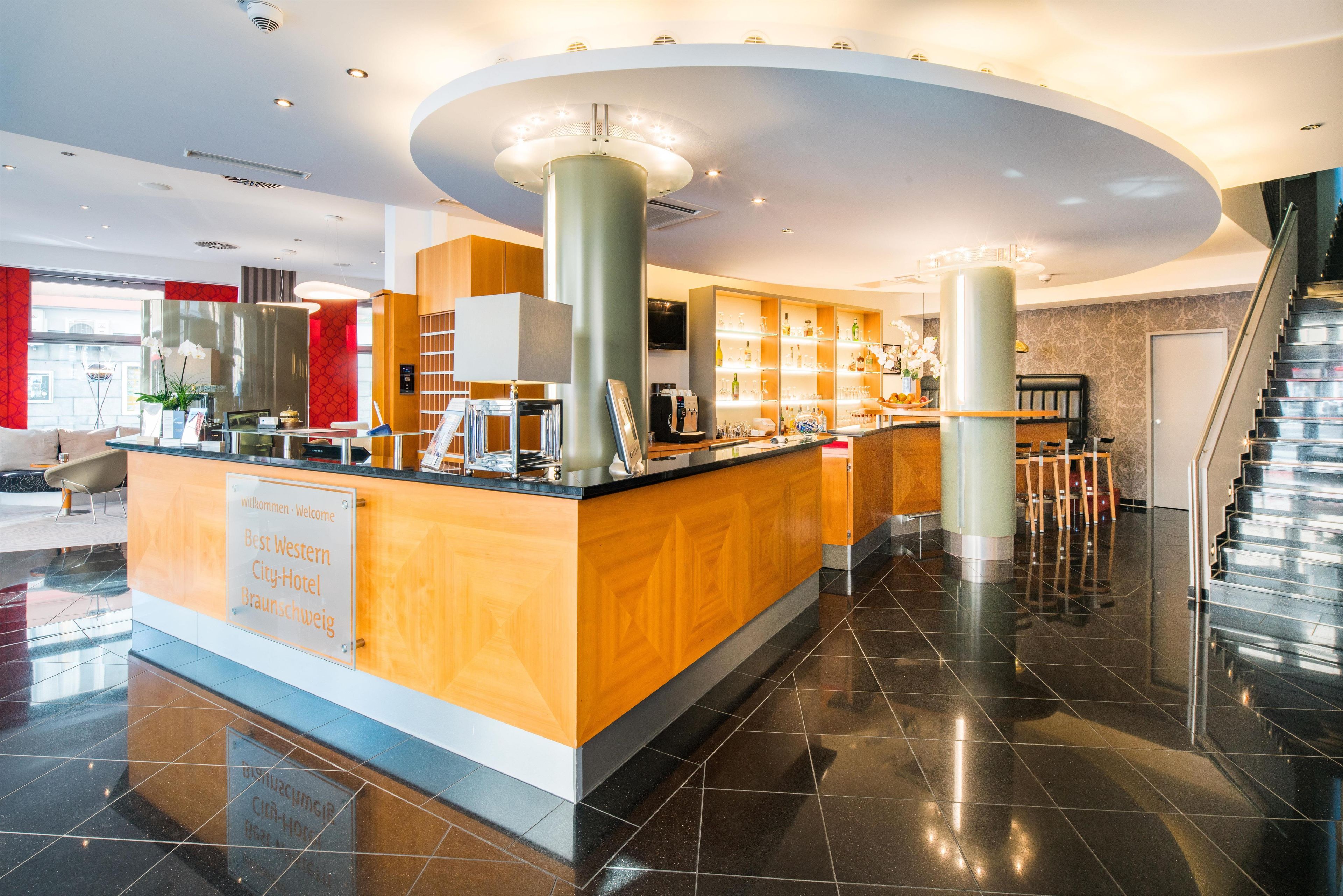Un moderno vestíbulo de hotel con mostrador de recepción, escalera y zona de bar.