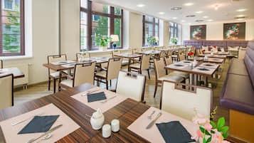 A hotel dining area with multiple tables set for guests, large windows, and a view of the outdoors.