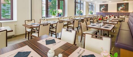 A hotel dining area with multiple tables set for guests, large windows, and a view of the outdoors.