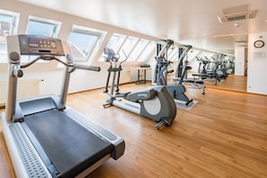 A gym with multiple exercise machines, large windows, and a wooden floor. - Best Western City-Hotel Braunschweig (Braunschweig)