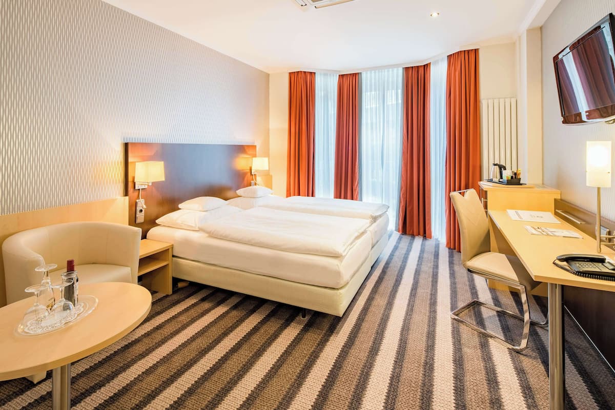 Habitació d'hotel amb un llit, escriptori, cadira, televisió i finestra amb cortines.