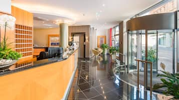 Eine moderne Hotelhalle mit einer Rezeption, einer Sitzecke und einem Glaselevator.