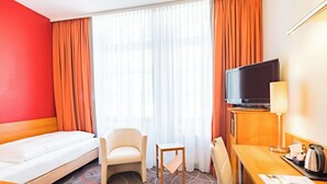 A hotel room with a bed, a chair, a small table, a television, and a desk with a lamp and a coffee maker. - Best Western City-Hotel Braunschweig (Braunschweig)