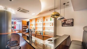 A modern bar area with a bar counter, stools, shelves with bottles, and a hanging pendant light.