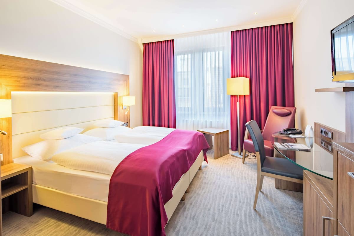 Una habitació d'hotel amb un llit gran, una taula de treball, una cadira i una televisió.