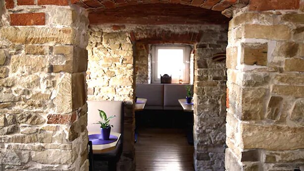 A narrow stone corridor with a brick archway, a window with a view, and a table with a potted plant. - Hotel Westerkamp (Osnabrueck)