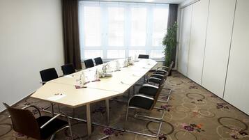 Une salle de conférence avec une longue table, des chaises et une grande fenêtre équipée de stores.