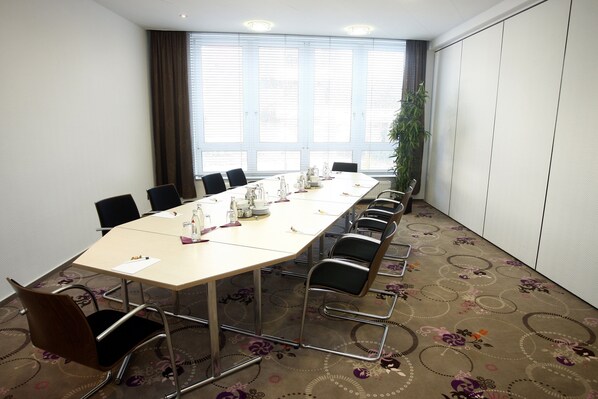 Un salón de conferencias con una larga mesa, sillas y un amplio ventanal con persianas.