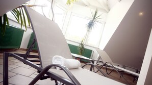 A sun lounger with a towel, a green radiator, and a window with plants. - Hotel Westerkamp (Osnabrueck)