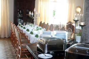 Un comedor con una larga mesa dispuesta para una comida, rodeada de sillas, con una barra de buffet y candelabros.