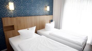 A hotel room with two single beds, a wooden headboard, and patterned wallpaper.