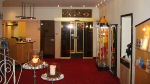 A hotel lobby with a red carpet, a reception desk, a glass elevator, and a glass display case with items. - City Hotel by Celina (Hagen)