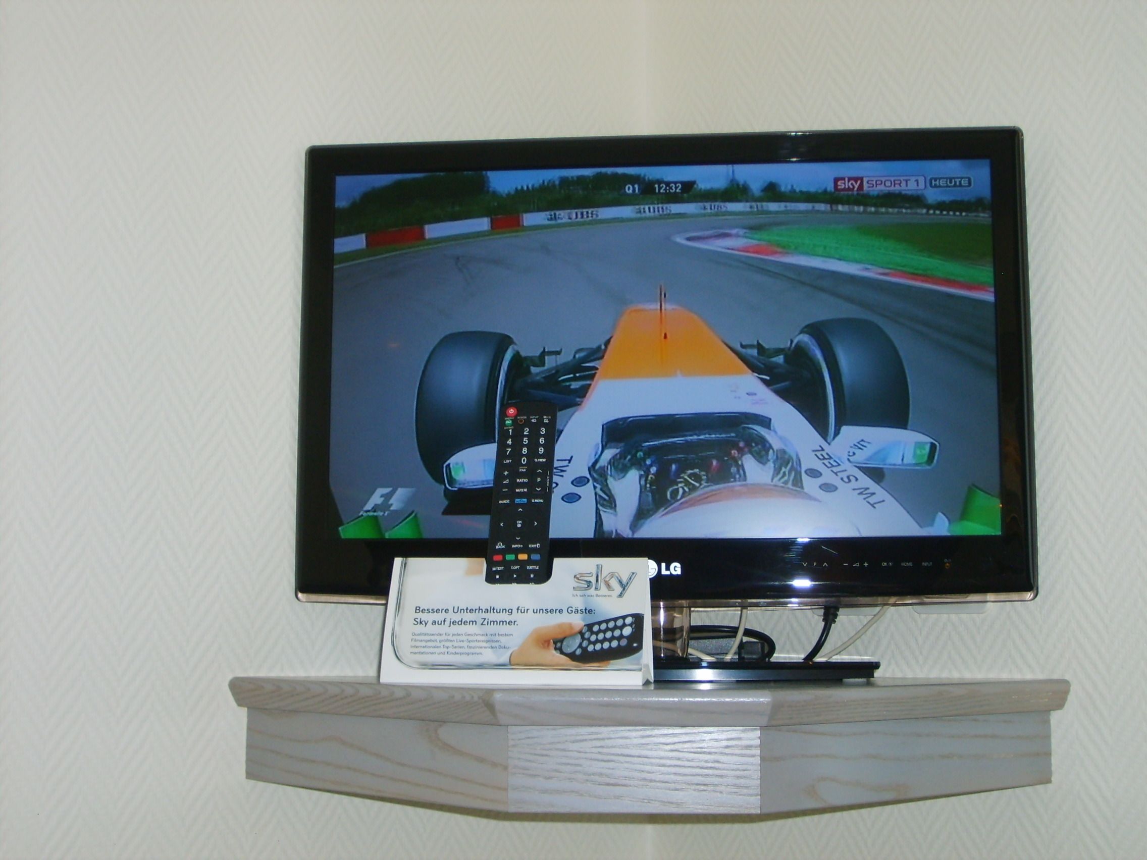 Un téléviseur affichant un jeu de course, fixé au mur, avec une télécommande et une boîte publicitaire placée en dessous.