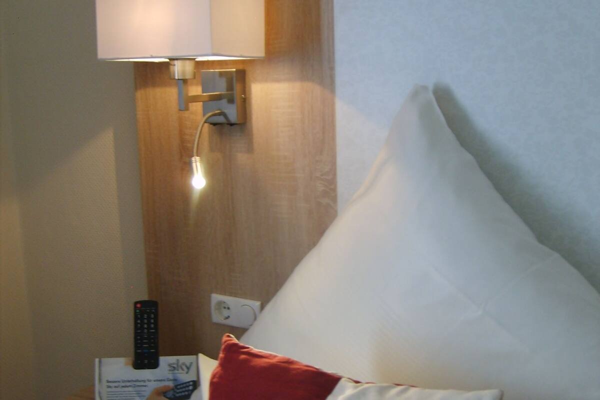 A hotel room with a bed, a nightstand, a lamp, a remote control, and a pillow.