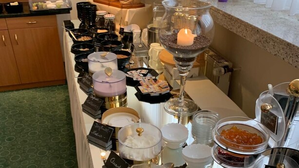 A buffet setup with various food items and condiments, including a bowl of fruit salad, jars of jam, and a candle on the table. - City Hotel by Celina (Hagen)