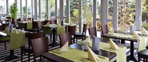 A restaurant with tables set for dining, featuring a view of trees and foliage through large windows. - Hotel Ambiente Walldorf (Walldorf)