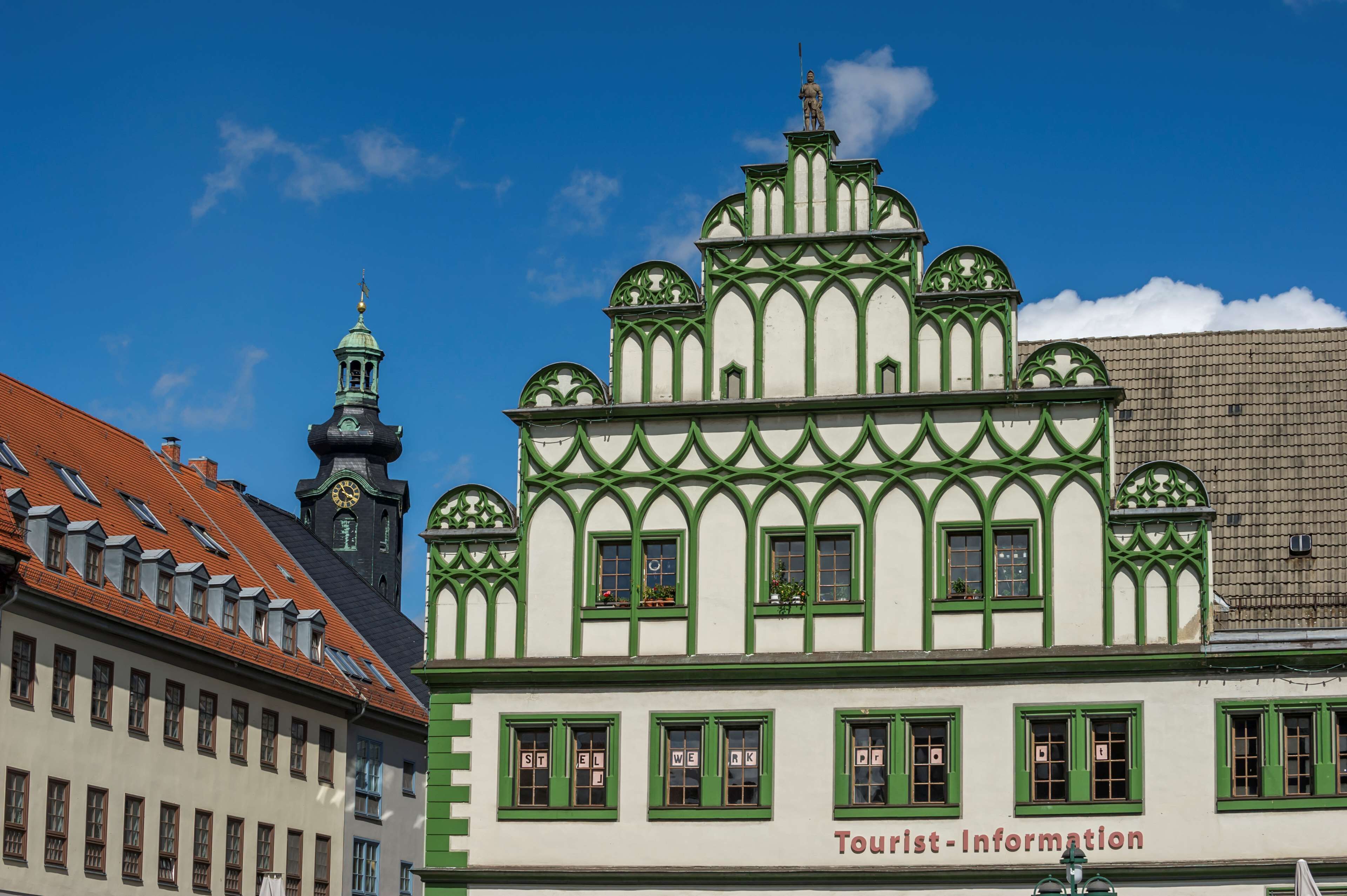 A building with a green and white facade, a clock tower, and a sign for tourist information.