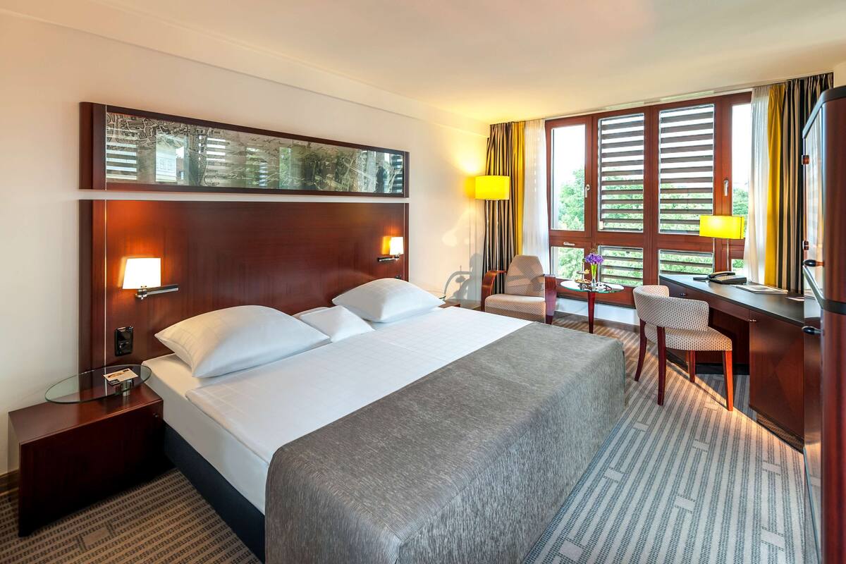 A hotel room with a large bed, a desk, a chair, and a wardrobe.