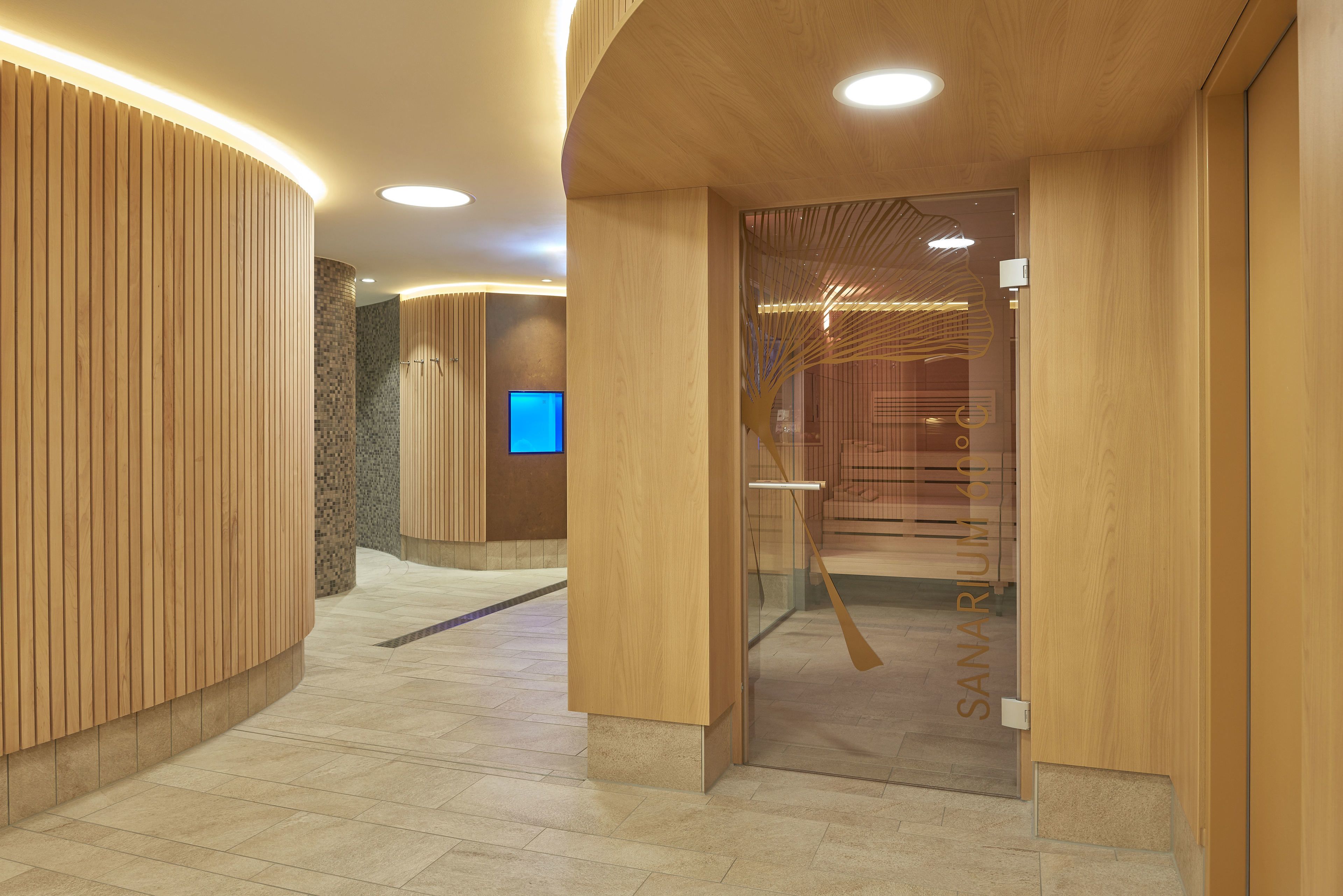 A modern hotel lobby with wooden paneling, a reception desk, and a glass door leading to a room.