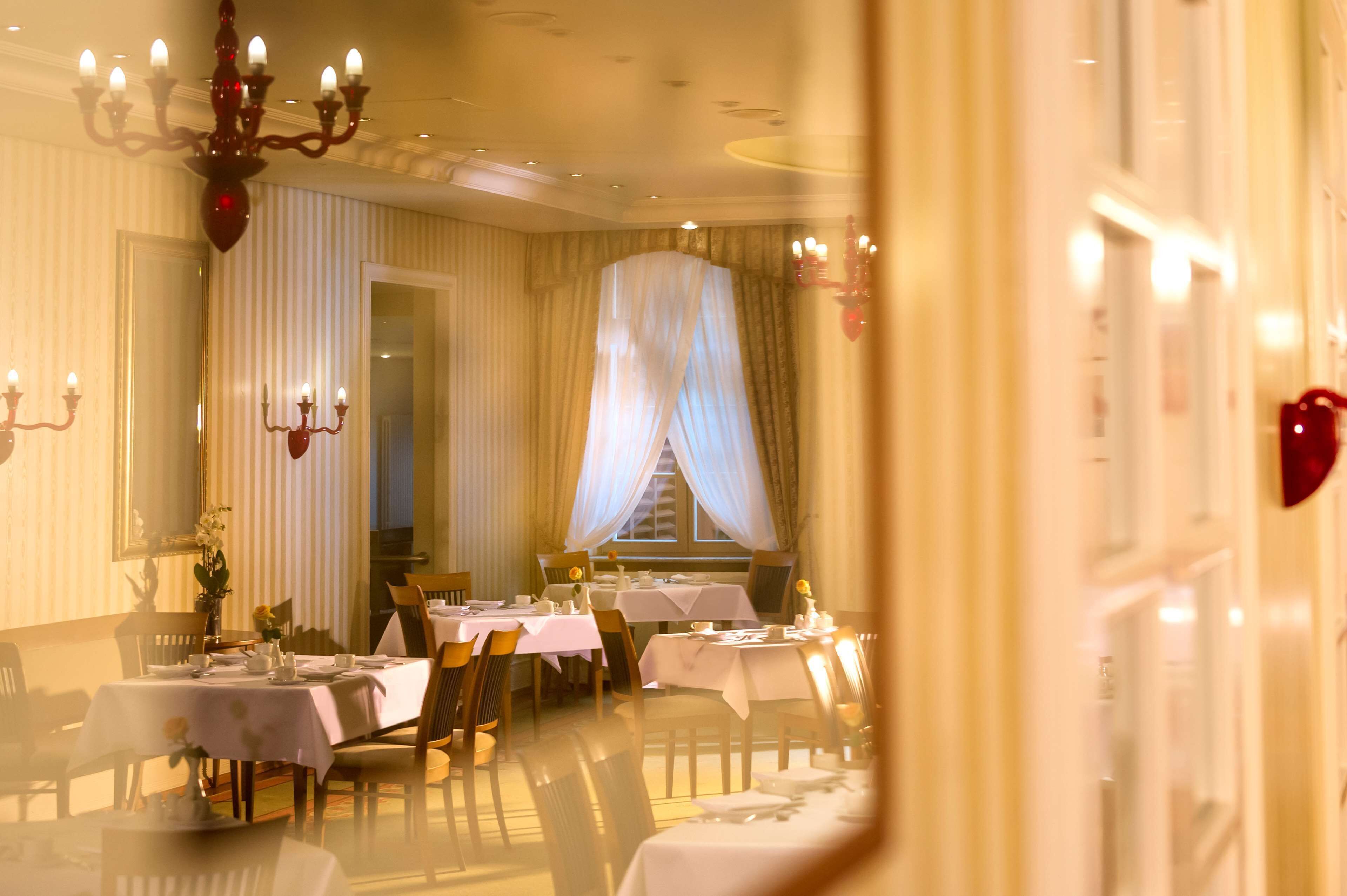 A dining area with tables set for a meal, a chandelier, and a window with curtains.