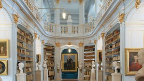 Una biblioteca majestuosa con arquitectura ornamentada, techos altos y extensas colecciones de libros.