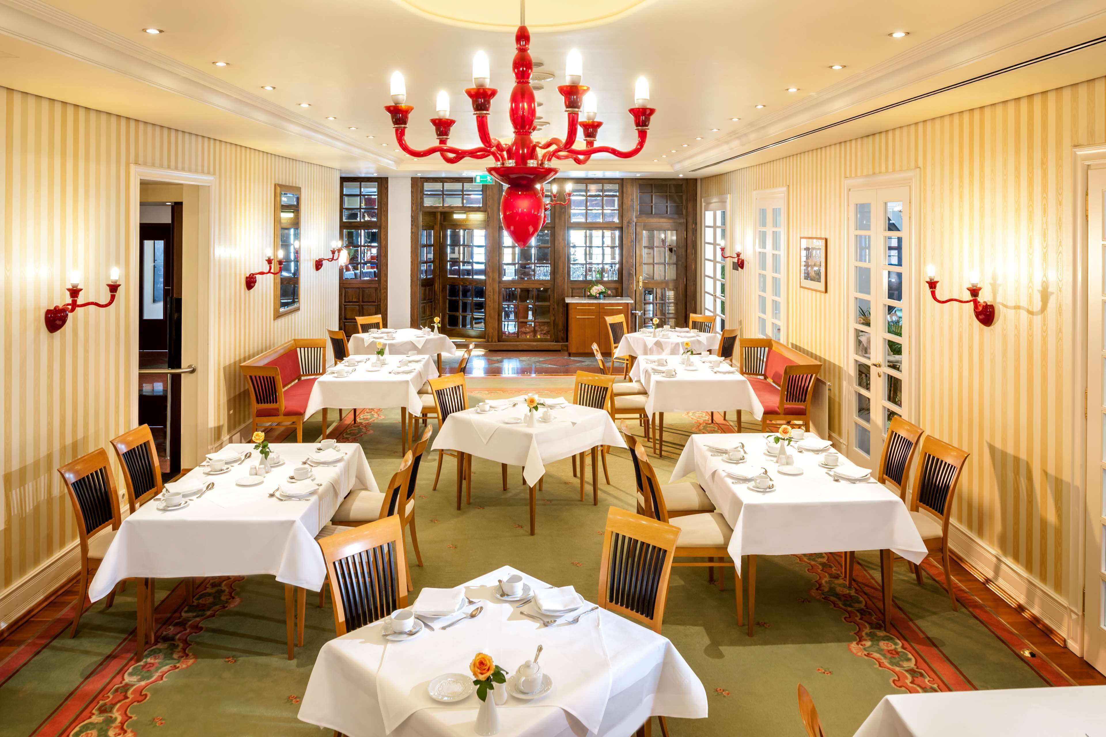 Uma sala de jantar com várias mesas preparadas para o serviço, um candelabro e papel de parede listrado.