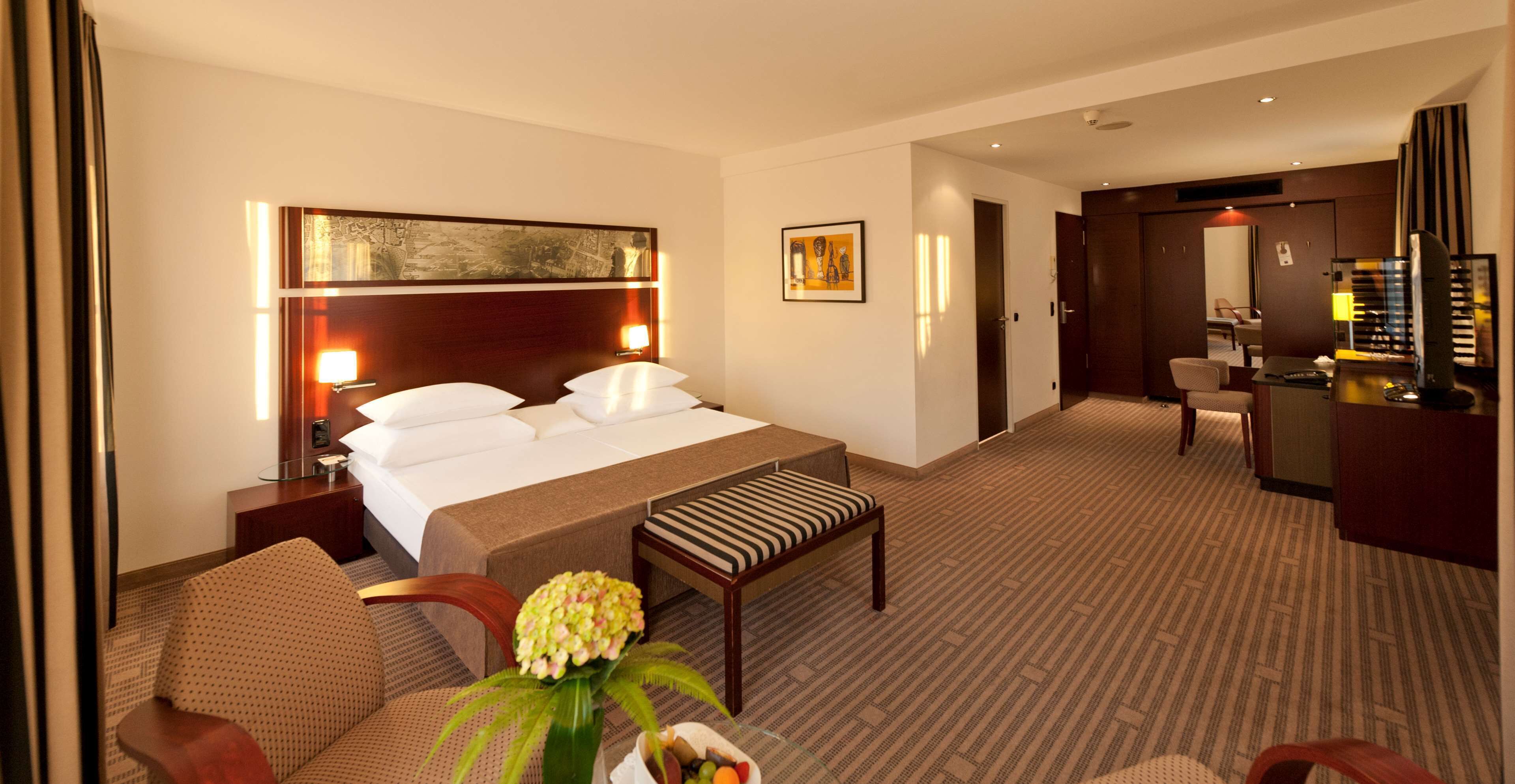 Ein Hotelzimmer mit einem großen Bett, einem Schreibtisch, einem Sessel, einem kleinen Tisch und einer Blumenvase.